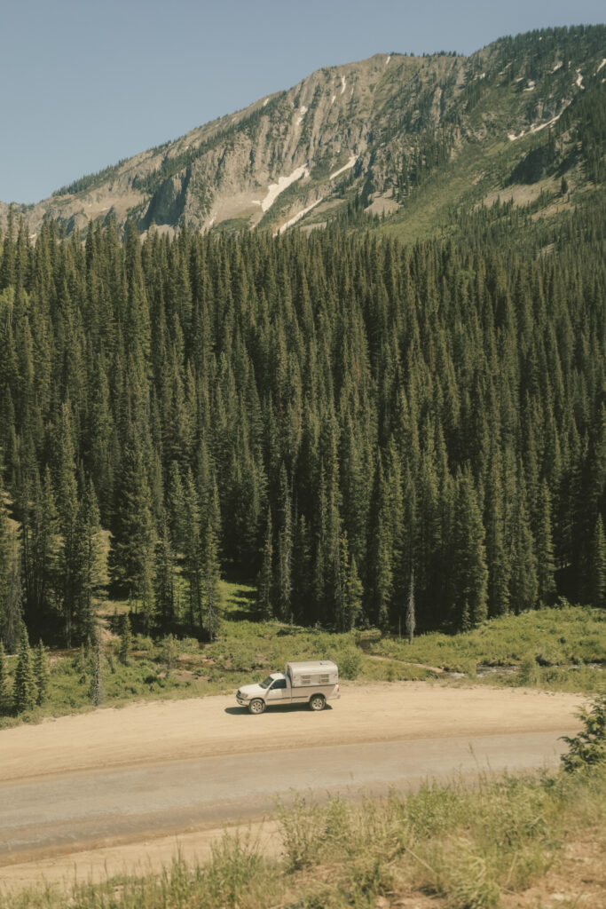 A white tundra and truck camper alongside a road in Colorado with green trees in the back and a mountain behind that.