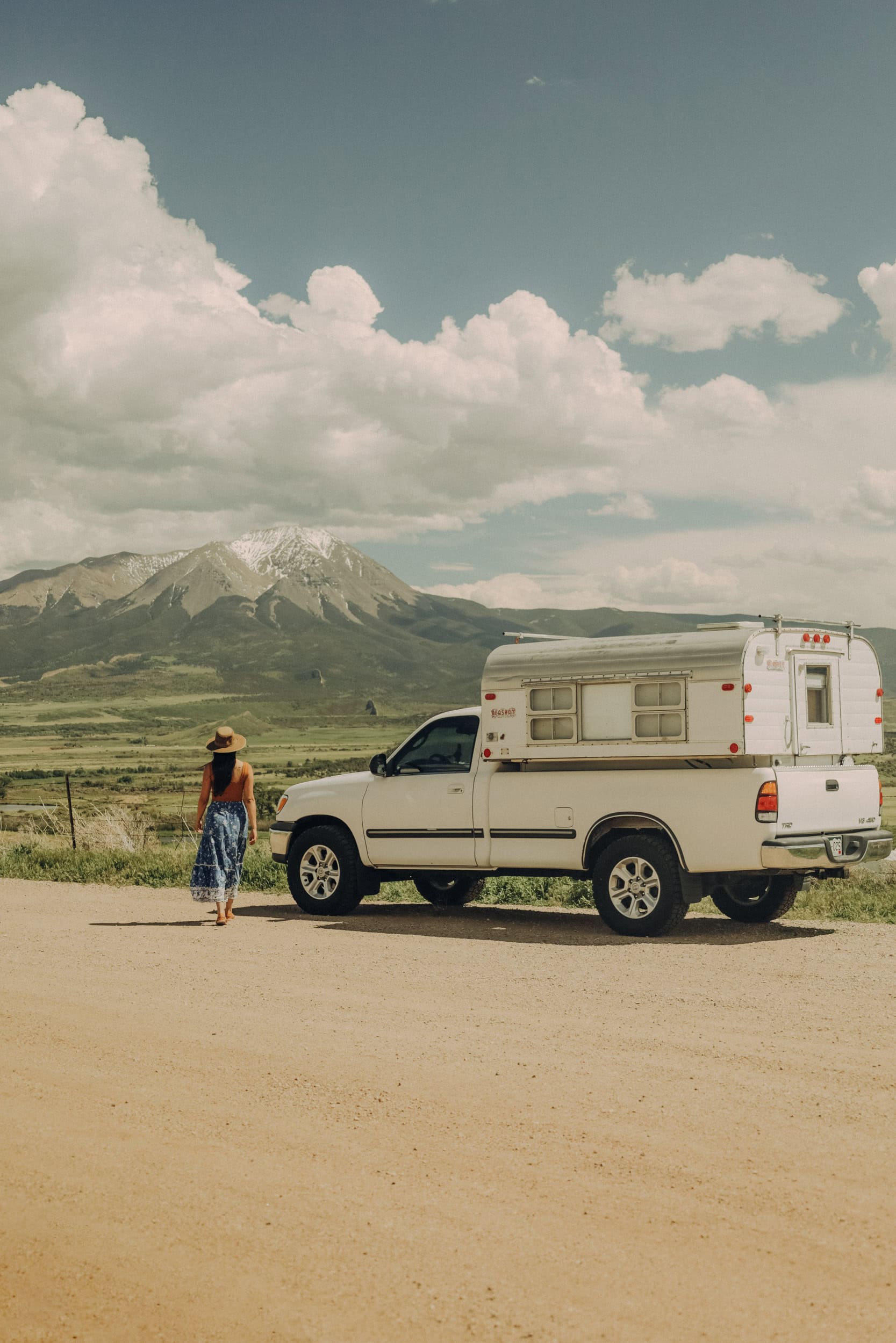 A girl named Jessy standing by her white truck camper standing in front of Spanish Peaks, Colorado on a day trip